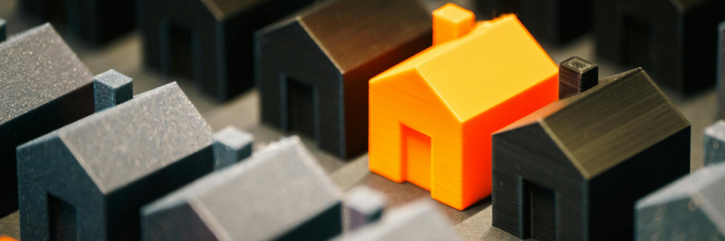 Casas en miniatura con una vivienda destacada en color naranja, representación del mercado inmobiliario y la tributación del IVA en vivienda protegida y derecho de superficie.