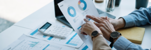 Persona analizando informe financiero con gráficos circulares y datos de marketing digital en oficina con portátil, calculadora y documentos de analítica, concepto de gestión empresarial y estrategia en España.